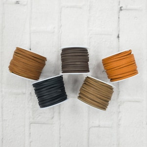 May include: Five spools of leather cord in different colors: brown, black, orange, tan, and dark brown. The spools are arranged in a semi-circle on a white brick background.