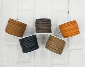 May include: Five spools of leather cord in different colors: brown, black, orange, tan, and dark brown. The spools are arranged in a semi-circle on a white brick background.