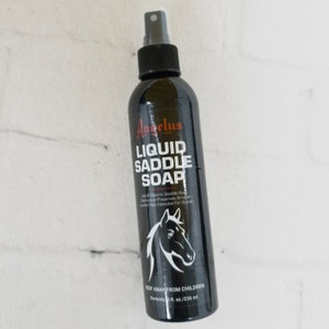 May include: A black bottle of Angelus Liquid Saddle Soap with a red label and a horse silhouette. The label reads "Liquid Glycerin Saddle Soap Cleans and Preserves Smooth Leather Not Intended For Suede" and "Keep Away From Children". The bottle contains 8 fl. oz. / 236 ml.