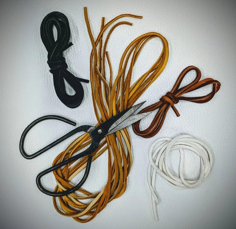 May include: A close-up of a set of leather cords in brown, white and black, with a pair of scissors. The cords are arranged in a starburst pattern, with the scissors in the centre.