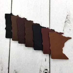 May include: A set of eight leather Minnesota state outline shapes in various shades of brown, black, and burgundy.