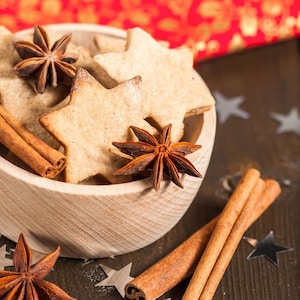 May include: A wooden bowl filled with star-shaped cookies and cinnamon sticks. The bowl is surrounded by star-shaped sprinkles and two cinnamon sticks.