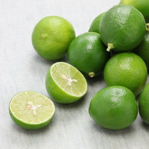 May include: A group of green limes, some whole and some cut in half, on a white textured surface.