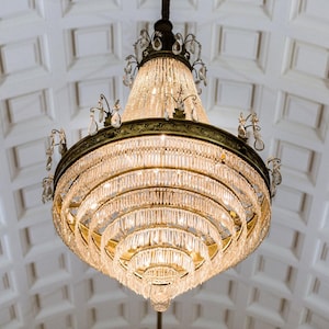 May include: A large, ornate, crystal chandelier with multiple tiers of hanging crystals. The chandelier is made of gold metal and has a traditional design.