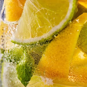May include: Close-up of a refreshing drink with lime, orange, and mint leaves. The drink is bubbly and has a yellow hue.