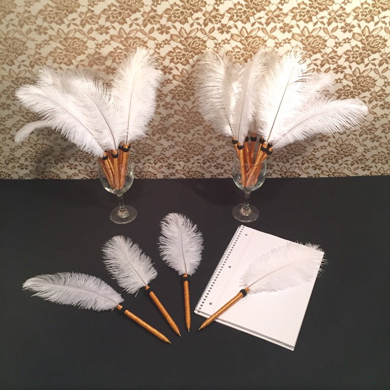 May include: A set of white feather pens with gold barrels. The pens are arranged in two vases and on a notebook.