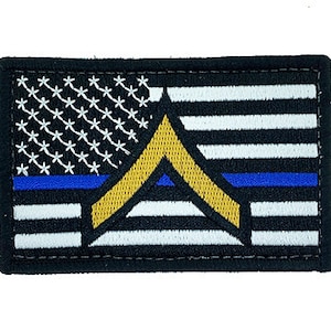 May include: Embroidered patch featuring a stylized American flag with a blue line and a gold chevron. The flag has black and white stripes, a blue line, and a field of white stars on a black background. The patch is rectangular.