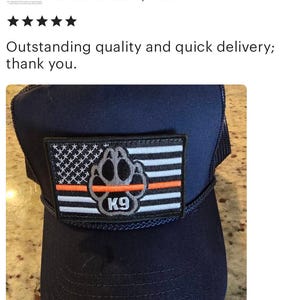 May include: A navy blue trucker hat with a black and white American flag patch featuring a paw print and the text "K9". The patch also has a thin orange stripe.