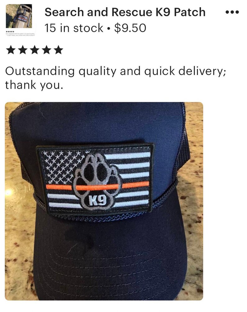 May include: A navy blue trucker hat with a black and white American flag patch featuring a paw print and the text "K9". The patch also has a thin orange stripe.