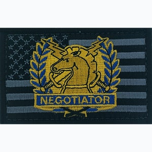 May include: A black and gray embroidered patch with an American flag background. The patch features a gold horse head with a lightning bolt and swords, surrounded by blue laurel leaves. The text "NEGOTIATOR" is written in gold below the horse head.