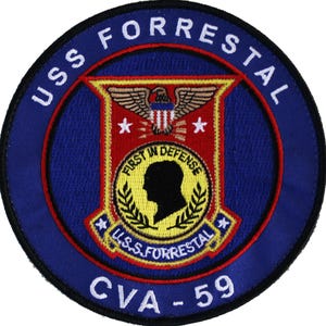 Könnte beinhalten: Ein kreisförmiger Aufnäher mit blauem Hintergrund und weißem Text, der "USS FORRESTAL" oben und "CVA-59" unten zeigt. In der Mitte befindet sich ein rotes und goldenes Emblem mit einem Adler, Sternen und den Worten "FIRST IN DEFENSE".