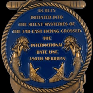 May include: A bronze-colored medallion with a blue center, featuring text and mermaid illustrations. The text reads "AS DULY INITIATED INTO THE SILENT MYSTERIES OF THE FAR EAST HAVING CROSSED THE INTERNATIONAL DATE LINE 180TH MERIDIAN".