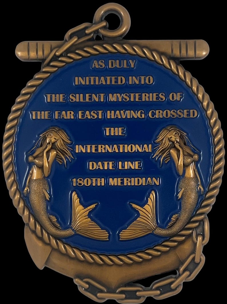 May include: A bronze-colored medallion with a blue center, featuring text and mermaid illustrations. The text reads "AS DULY INITIATED INTO THE SILENT MYSTERIES OF THE FAR EAST HAVING CROSSED THE INTERNATIONAL DATE LINE 180TH MERIDIAN".