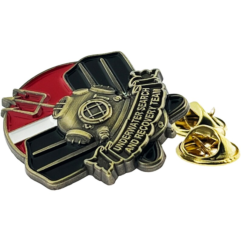 May include: A gold-toned metal pin with a black and red design. The pin features a diving helmet, a trident, and a banner that reads "Underwater Search and Recovery Team".