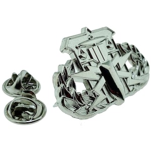 May include: Silver military badge with a shield, lightning bolts, and a laurel wreath. The badge is attached to a pin back.