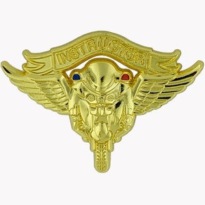Puede incluir: Pin de instructor de motocicleta de color dorado con alas y la palabra "INSTRUCTOR" en una pancarta arriba. La motocicleta tiene detalles rojos y azules.