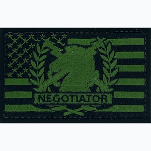 May include: Green embroidered patch with an American flag background. The patch features a soldier holding a rifle with a laurel wreath around the soldier. The text "NEGOTIATOR" is below the soldier.