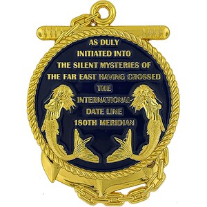 May include: A gold-colored metal medallion with a dark blue center, featuring text and two mermaids. The text reads "AS DULY INITIATED INTO THE SILENT MYSTERIES OF THE FAR EAST HAVING CROSSED THE INTERNATIONAL DATE LINE 180TH MERIDIAN". An anchor and chain are at the bottom.