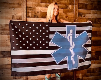 May include: A black and white American flag with a blue and white medical star of life symbol. The flag is being held by a person.