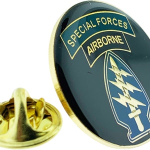 Op de afbeelding: Een gouden pin met een zwarte achtergrond en een groen-gouden lint met de tekst "Special Forces Airborne". De pin heeft een blauwe en gouden bliksem met een zwaard.