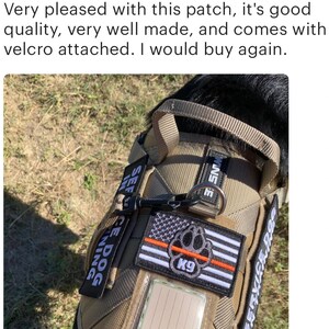 May include: A tan service dog vest with black straps and a black handle. The vest has a black and white American flag patch with a red paw print and the word "K9" in white. The vest also has two patches that say "Service Dog" and "K9" in white.