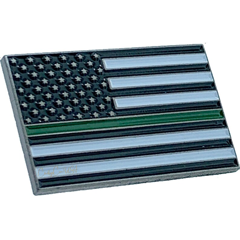 Pode incluir: Um alfinete de metal fino com uma linha verde no meio da bandeira americana. A bandeira &eacute; preta e branca com uma linha verde no meio.