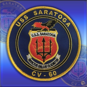 May include: A circular navy blue patch with gold trim, featuring the text "USS SARATOGA" and "CV-60". The patch includes a central emblem with a trident and the words "INVICTUS GALLUS GLADIATOR".