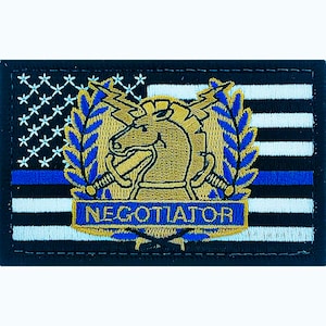 May include: A black and white American flag patch with a blue line, featuring a gold embroidered image of a horse's head with a crown and swords, surrounded by a laurel wreath. The text "NEGOTIATOR" is embroidered in gold below the image.
