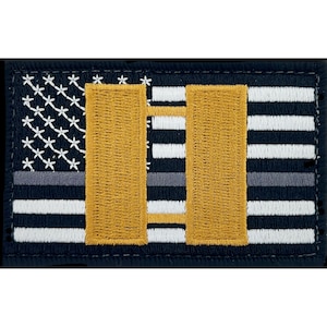 Könnte beinhalten: Ein schwarzer und weißer amerikanischer Flaggen-Patch mit einer dünnen blauen Linie und einem goldenen Balken, der den Rang eines Militäroffiziers darstellt.