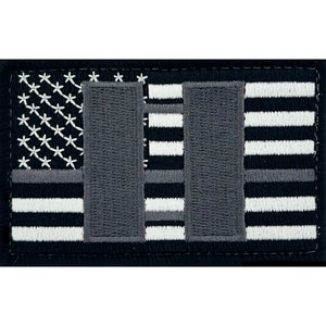 May include: Black and white embroidered patch with a thin blue line American flag design. The flag has two grey vertical bars in the centre.