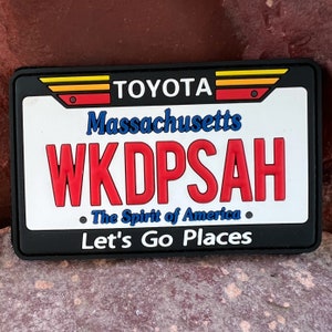 May include: Black and white license plate style patch with red, yellow, and orange accents. The patch says "TOYOTA", "Massachusetts", "WKDPSAH", "The Spirit of America", and "Let's Go Places".