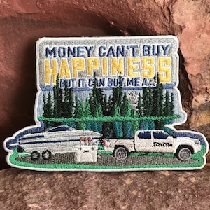 Puede incluir: Parche bordado con una camioneta blanca remolcando un barco. El parche tiene el texto "El dinero no puede comprar la felicidad, pero puede comprarme un..." con una escena de bosque en el fondo.