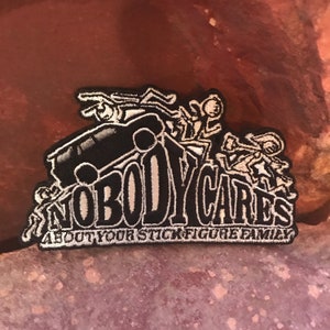 Puede incluir: Parche bordado en blanco y negro con el texto "Nobody Cares About Your Stick Figure Family". El parche presenta un coche de dibujos animados con personas de palo que se caen de él.