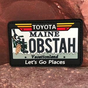 May include: Black and white patch with a cartoon lobster and the text "Maine Lobstah" on a white background. The patch also has the text "Toyota Vacationland Let's Go Places".