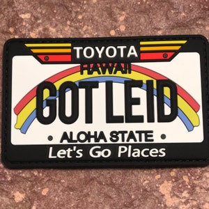 May include: Black and white patch with a rainbow design and the text "TOYOTA HAWAII GOT LEID ALOHA STATE Let's Go Places".