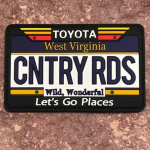 May include: Black and yellow patch with a white license plate that says "CNTRY RDS" and the text "Toyota West Virginia Wild, Wonderful Let's Go Places".
