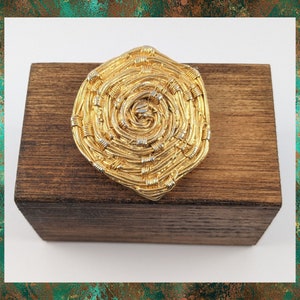 May include: A gold-toned brooch with a spiral design. The brooch is made of woven wire and has a textured surface.