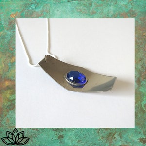 May include: A silver necklace with a blue gemstone pendant. The pendant is shaped like a boat and the gemstone is set in the centre.