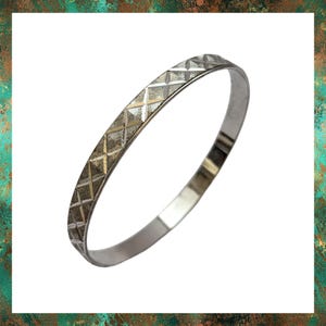 May include: A silver bangle bracelet with a geometric pattern. The bracelet is smooth and shiny.