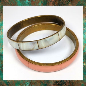 May include: Two brass bangles, one with a white mother-of-pearl inlay and the other with a pink enamel finish.