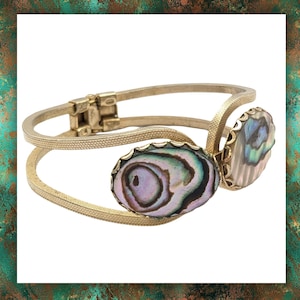 May include: A gold-toned bangle bracelet with two oval-shaped abalone shell accents. The shell has iridescent colours of green, purple, and blue.