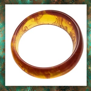 May include: A translucent, amber-coloured bangle bracelet. The bracelet has a marbled effect with shades of yellow and brown. The smooth, rounded design suggests a vintage or retro style. The bangle is a single, continuous loop.