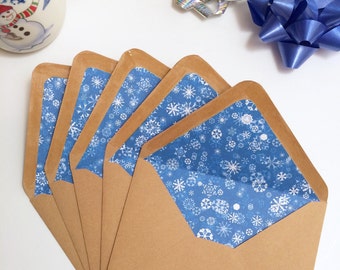 May include: Five brown envelopes with blue snowflake patterned liners. The envelopes are arranged in a fan shape with the top envelope open to reveal the liner.