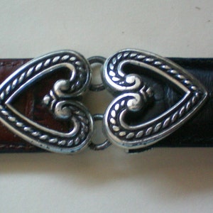 Peut inclure: Une ceinture en cuir marron et noir avec une boucle en forme de c&oelig;ur argent&eacute;e.