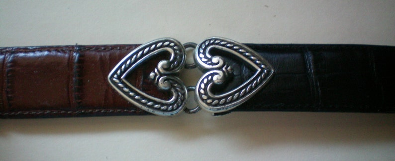 Peut inclure: Une ceinture en cuir marron et noir avec une boucle en forme de c&oelig;ur argent&eacute;e.