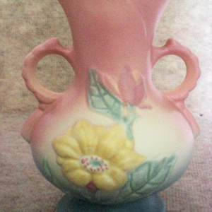 Puede incluir: Un jarrón de cerámica rosa y blanco con una base azul. El jarrón tiene un diseño floral con flores amarillas, rosas y verdes.
