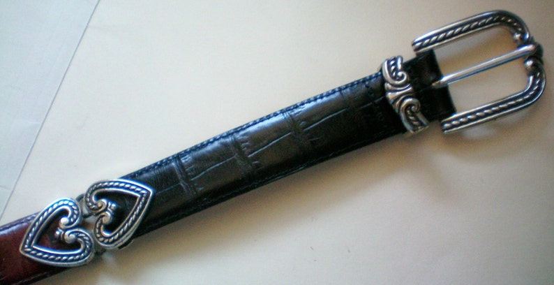 Peut inclure: Une ceinture en cuir noir avec une boucle argent&eacute;e et des accents en forme de c&oelig;ur. La boucle a un design d&eacute;coratif.