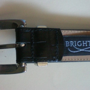 Peut inclure: Une ceinture en cuir noir avec une boucle argent&eacute;e et un logo Brighton. La ceinture a un motif crocodile et le logo est emboss&eacute; en argent.