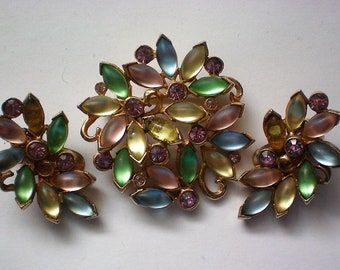 May include: A set of vintage jewelry featuring a brooch and earrings. The pieces are made of gold-tone metal and feature a floral design with pastel-colored stones. The brooch is larger than the earrings and has a more elaborate design.
