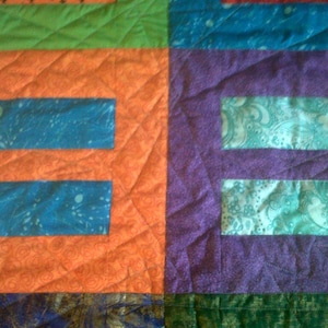 Puede incluir: Una colcha con un diseño de patchwork que presenta una variedad de colores y patrones. La colcha está hecha de cuadrados y rectángulos, y los colores incluyen naranja, verde, azul, morado y azul verdoso. La colcha está acolchada con un patrón de diamante.